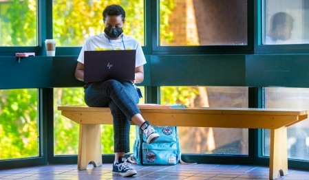 Student seated on a bench working on their laptop. 