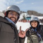 Two students smiling at the camera at the base of a ski slope. 
