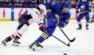 Action shot of a Buffalo Sabres player skating in the forefront controlling the puck with a player for the opposing team behind him trying to steal the puck.