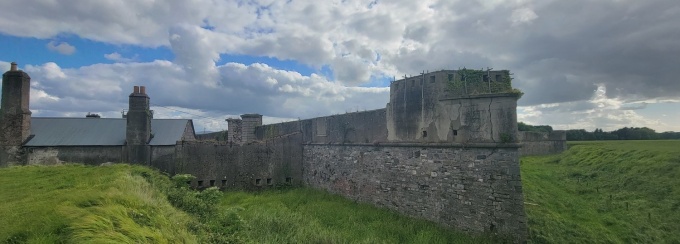 Long stone wall and house in an open field with cloudy sky. 