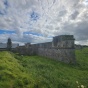 Long stone wall and house in an open field with cloudy sky. 