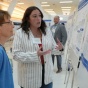 Student explaining their research to an onlooker in front of their poster. 