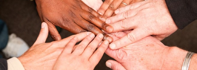 Photo of several hands of different skin colors stacked in partnership. 