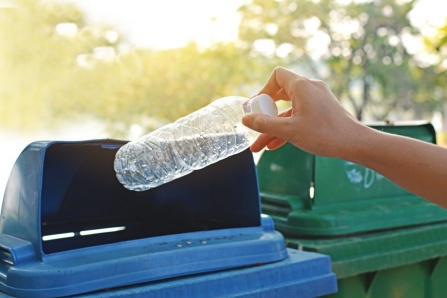 a plastic bottle being thrown into a recycling bin. 