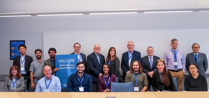 Seventeen people, a mix of male & Female sitting at a conference table smiling. 