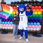 Victor E Bull posing with a student in front of a balloon progress pride wall. 