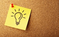 A hand-drawn image of a lightbulb on yellow post-it paper, pinned to a cork board. 