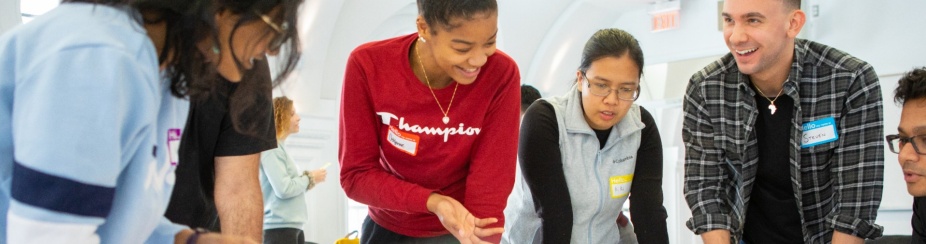 Students smiling and talking while working together around a table. 