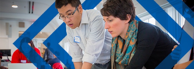 Two people standing over a laptop at the Global Health Equity group meeting in Hayes Hall on South Campus. 