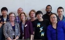 Photo image of 14 people of various ages, heights, genders, and ethnicities, standing in a confernce room, posing for the picture. These are members of the institute. 