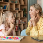 Professional woman speech therapist studying together with pretty little girl, learning practice pronunciation exercises. 