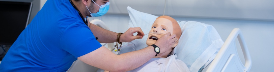 A medical student assisting a dummy in a hospital bed during a medical simulation. 