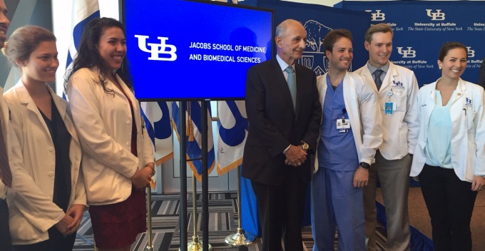 UB Council Chairman Jeremy M. Jacobs and UB medical students in front of a digital screen displaying the newly named "Jacobs School of Medicine and Biomedical Sciences". 