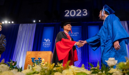 President Satish K. Tripathi shakes hands with a UB graduate as they cross the stage. 