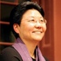 Photo of profile of a woman smiling. She has short hair, glasses, a black shirt, and a purple scarf. 