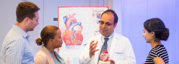 3 people standing around a man with a 3D heart diagram. 