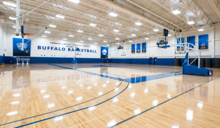 Wide view of the Ed Wright Practice Facility showing multiple basketball courts, polished wood flooring, hoops, and Buffalo Basketball branding throughout the indoor space. 