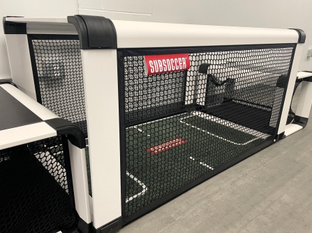 Subsoccer table featuring a miniature soccer field, goals, surrounding netting and seats for two players. 