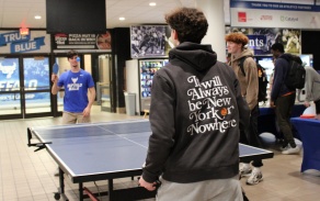 Two UB students play table tennis during Unplug & Play as other students gather nearby. 
