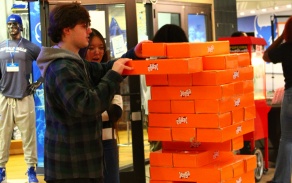 Two UB students carefully remove a block from a giant orange Jenga tower during Unplug & Play. 