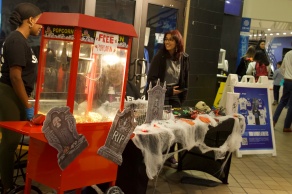 UB Recreation staff stand beside a free popcorn machine and a table decorated with cobwebs, tombstones, spiders and skulls for a Halloween event.