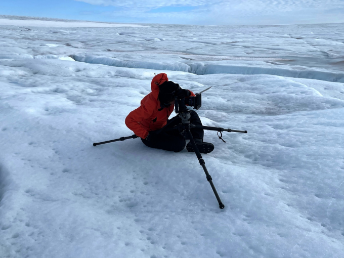Director sitiing on the Greenland Ice Sheet with camera on tripod. 