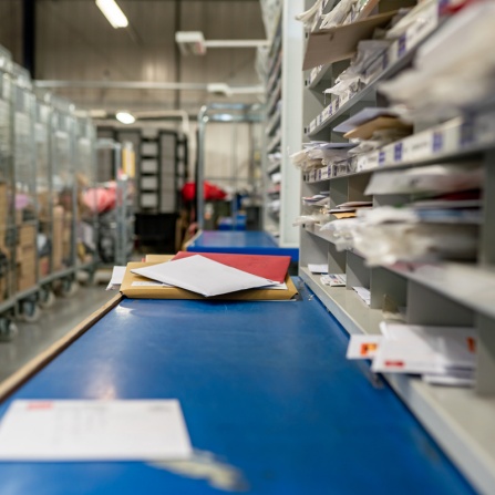 Pieces of mail going down conveyor belt to be scanned and sorted. 