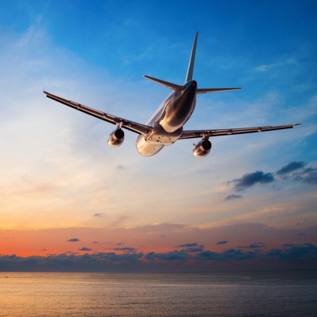 Airplane flying above ocean at sunset. 