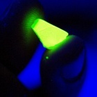 Neon green glowing material held in between two fingers in a dark room. 
