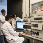 Students in lab coats using a computer in a facility on UB campus. 