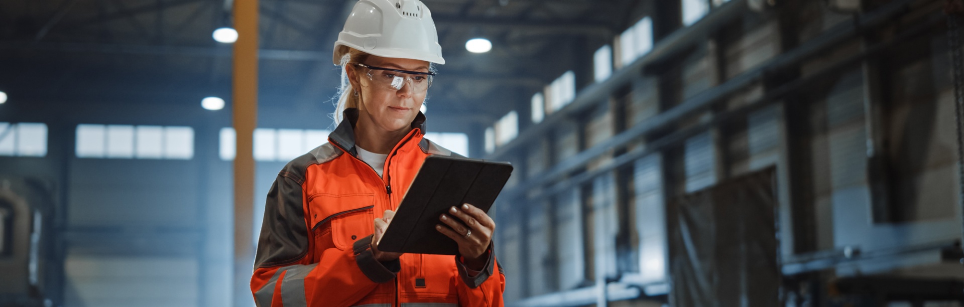 Female engineer entering data on a tablet wearing safety gear while standing in a warehouse. 