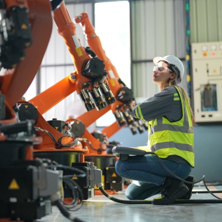 Female engineer testing industrial robotic arm in warehouse. 