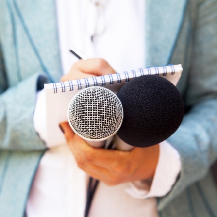 Reporter holding a microphone and taking notes during an interview. 