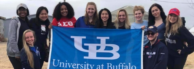 Students on an alternative break trip to the Louisiana wetlands pose with a blue UB flag outside of a service site. 