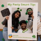 Three students decked out in St. Patrick's Day glasses and headbands offering their party safe tips to fellow students. 