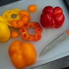 Yellow, orange and red peppers arranged on a cutting board with a knife. 