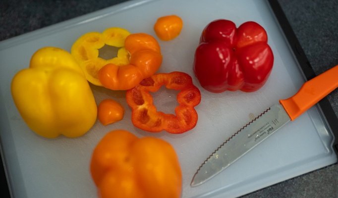 Yellow, orange and red peppers arranged on a cutting board with a knife. 