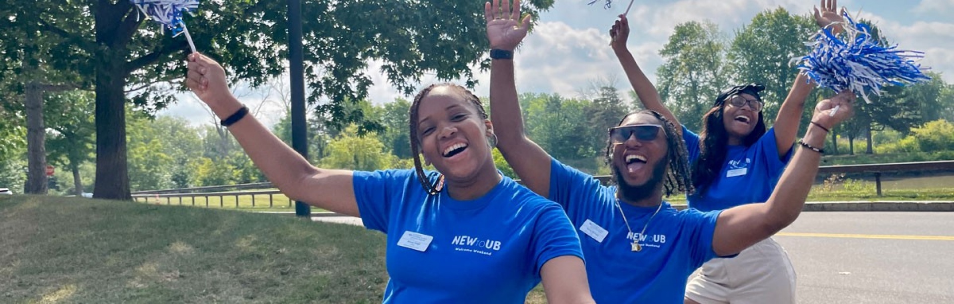 Four orientation leaders stand in the middle of a group circle during a game at a summer orientation session. All orientation leaders are wearing a version of khaki pants or shorts and their signature UB blue and white polos.