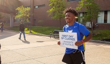 A student get a photo taken while holding a sign reading, "First Day of Classes.".