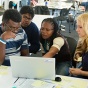 students gathered in front of a laptop, working together on a project. 