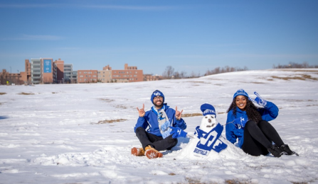 Two students with their snowperson dressed in UB hat and scarf. 