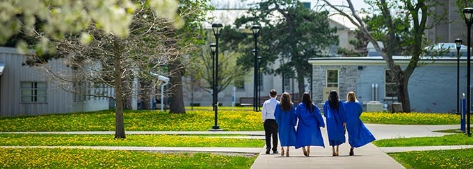Graduates in blue robes walk through South Campus in spring. 