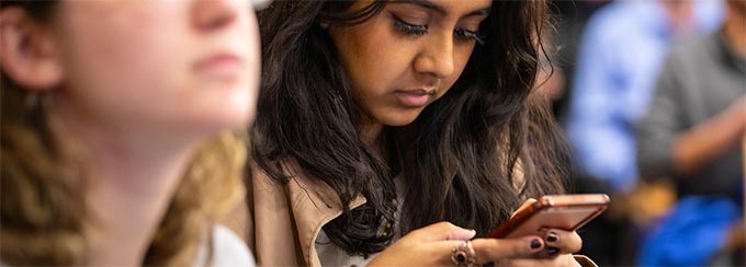 Student holding a smartphone with two hands and looking down at the screen.