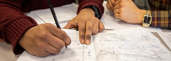 Hands of two students working on a problem in a notebook. 