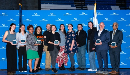Group of people standing in front of a backdrop holding awards. 