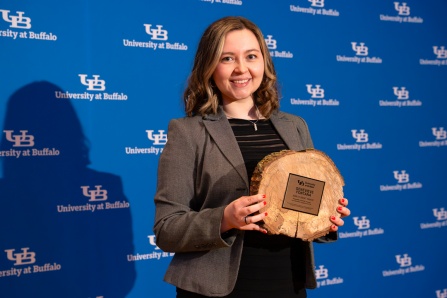 Genevieve Fontana holding the 2026 SLICE award in front of a UB logo background. 