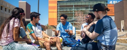 Five students sitting outside on a sunny day talking and laughing. 