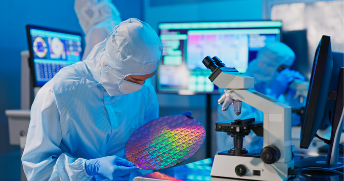 Man in cleanroom suit holding a large semiconductor wafer. 