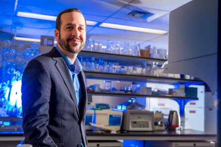Zoom image: Jonathan Lovell poses for a picture with lab equipment in the background.