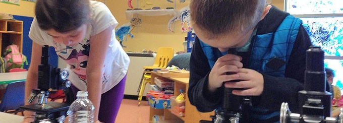 School age children looking at microscope. 